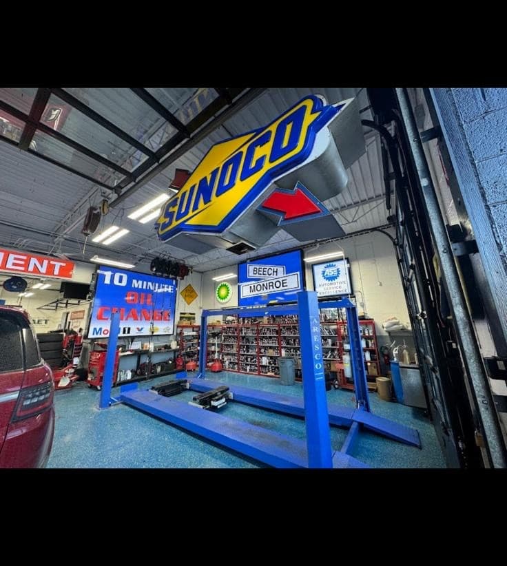 Large Sunoco sign hangs above a blue car lift in a busy auto repair garage.